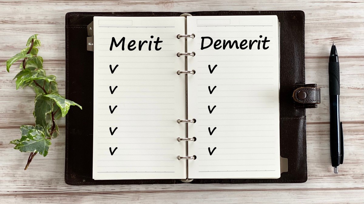 白板の上で開いた手帳とボールペンとツタ_俯瞰_MeritとDemeritの文字入り