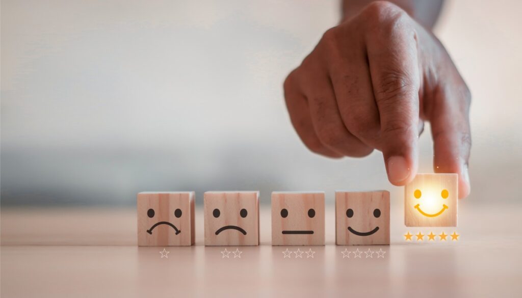 カスタマーサービス、最高のビジネス評価体験。満足度調査のコンセプト。ビジネスマンが木製ブロックのキューブに描かれたスマイリーフェイスを選んでいる。満足度5つ星